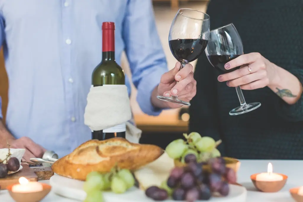 Glasses of red wine raised over a table of bread and fruit