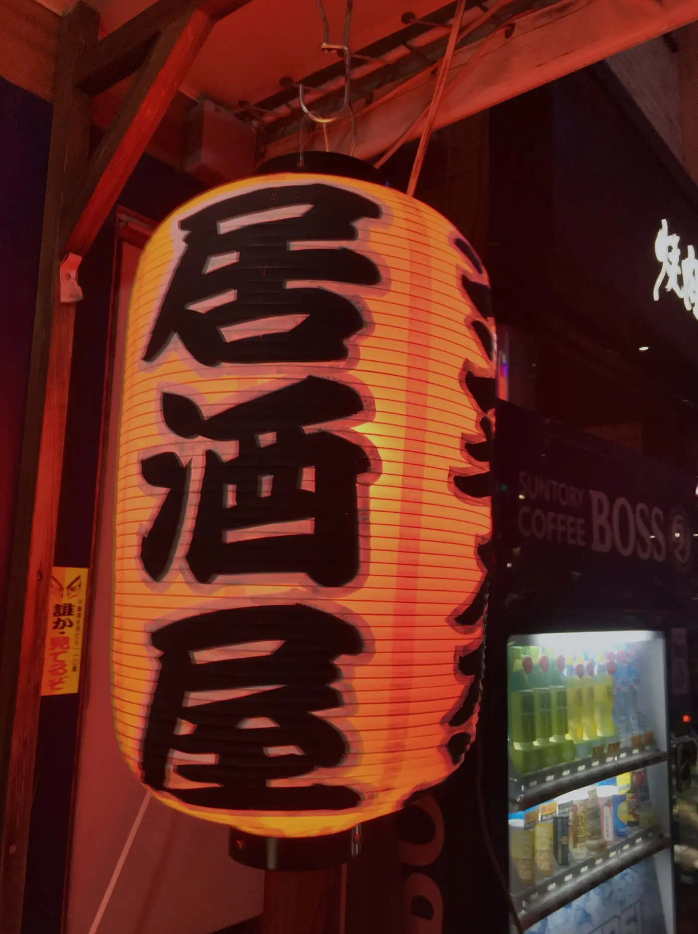 A red paper izakaya lantern glowing outside a doorway at night
