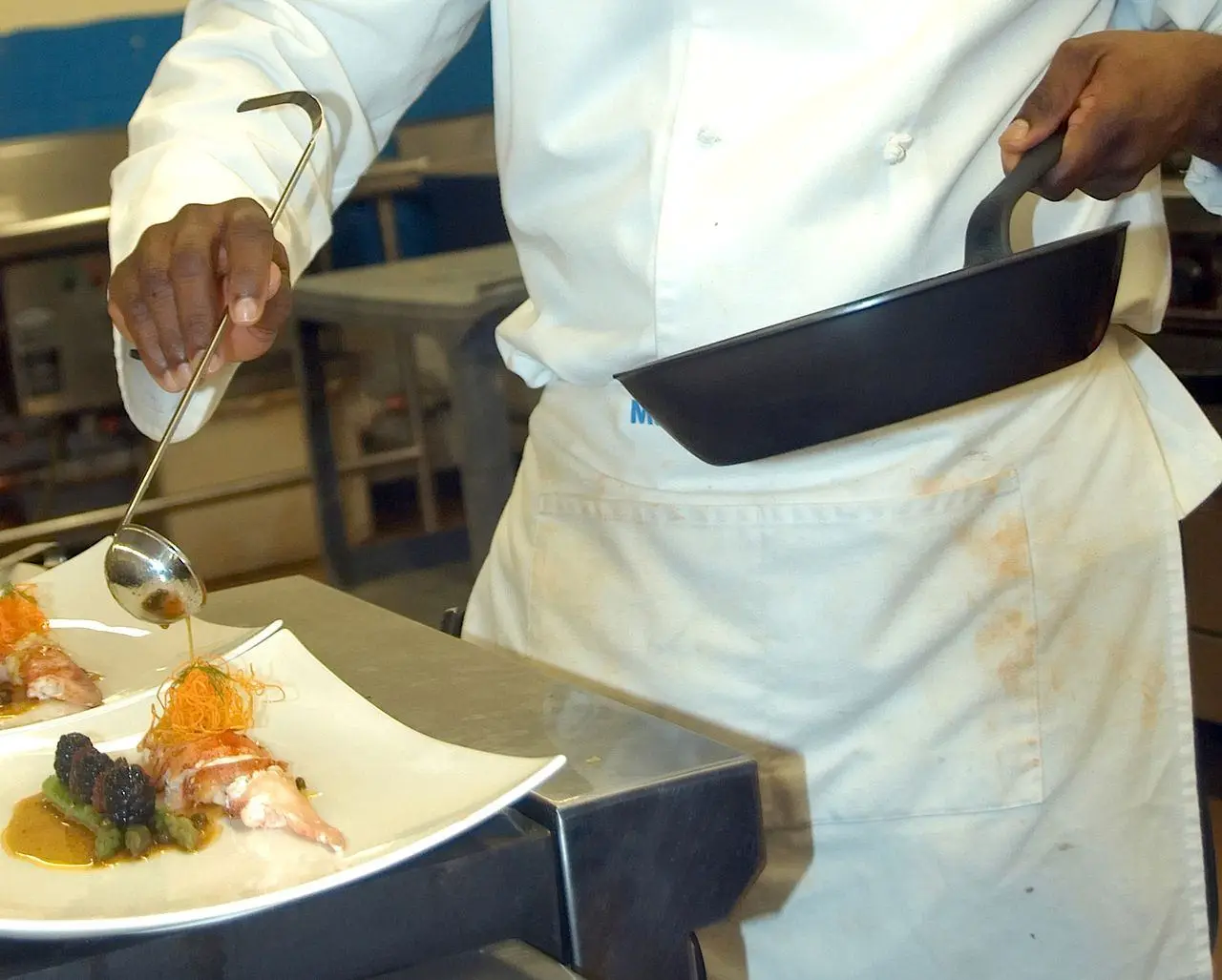 A chef spooning sauce over a plated course